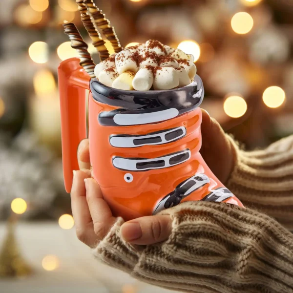 a holiday hot chocolate being served in an orange ceramic ski boot mug, complete with marshmallows.